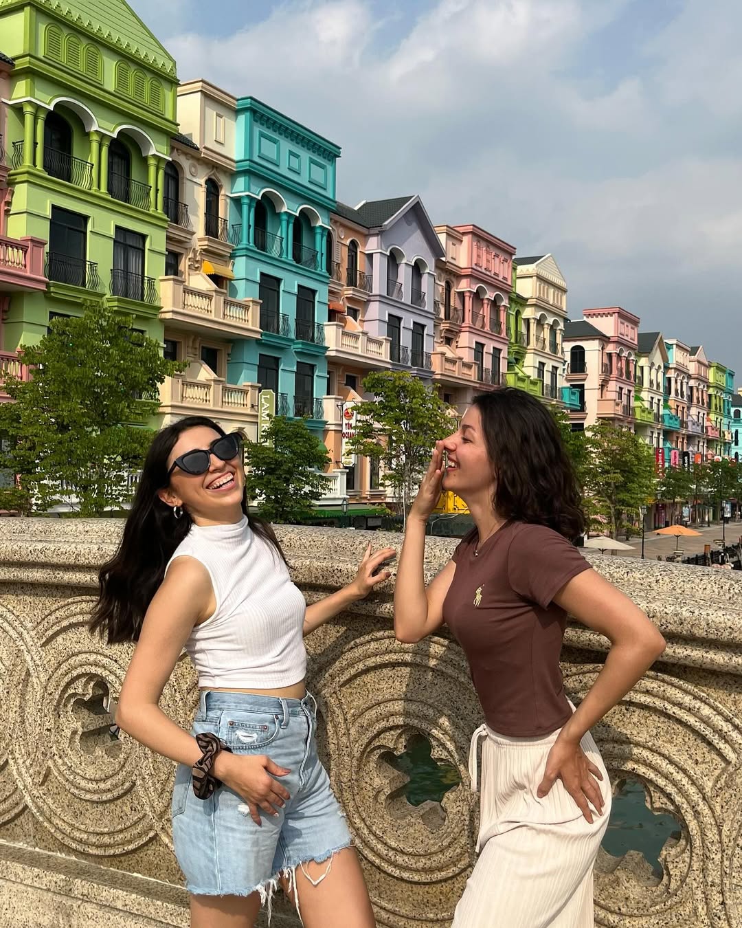 Bárbara and a friend laughing in front of colorful Vietnamese buildings