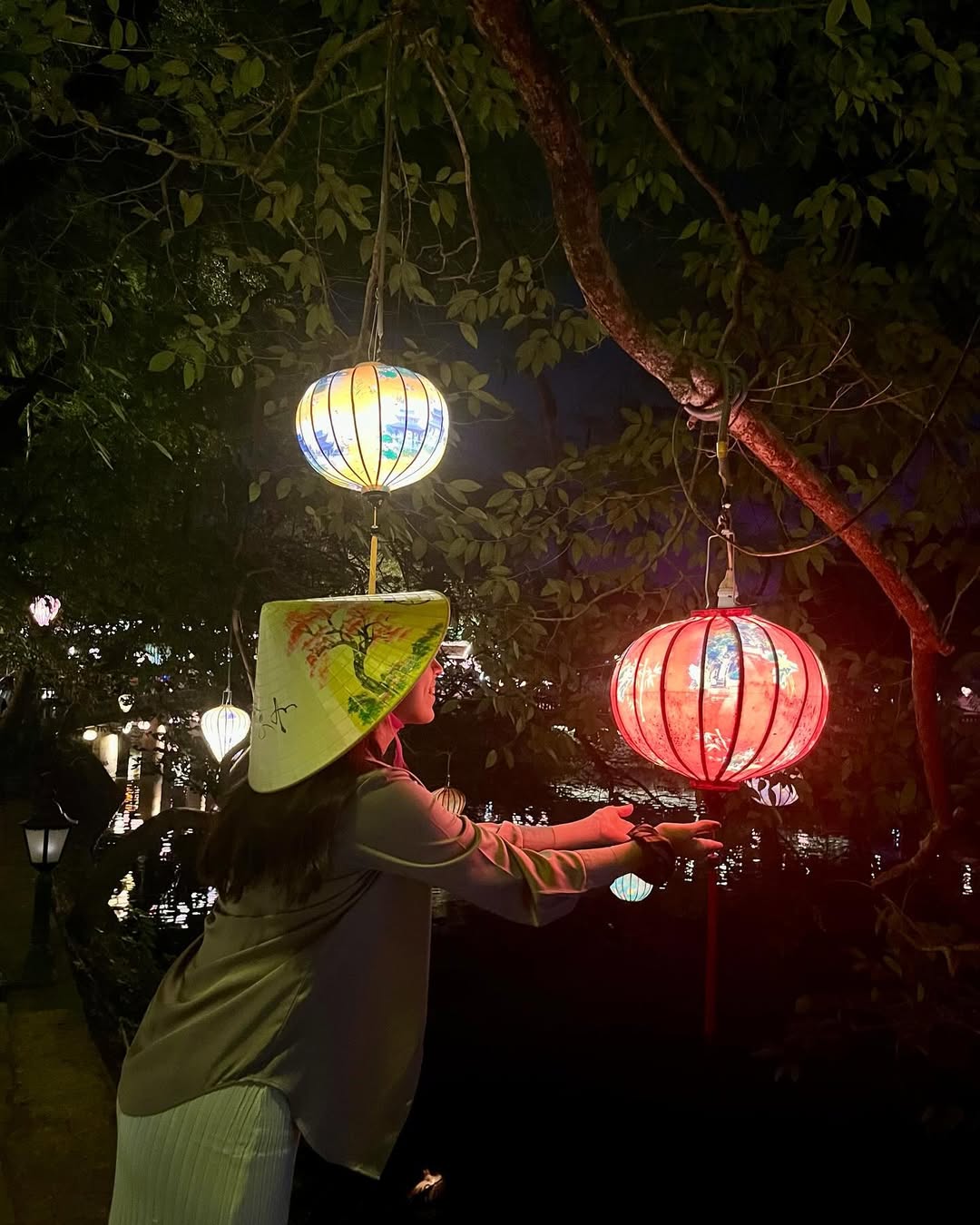 Bárbara reaching towards Vietnamese lanterns at night