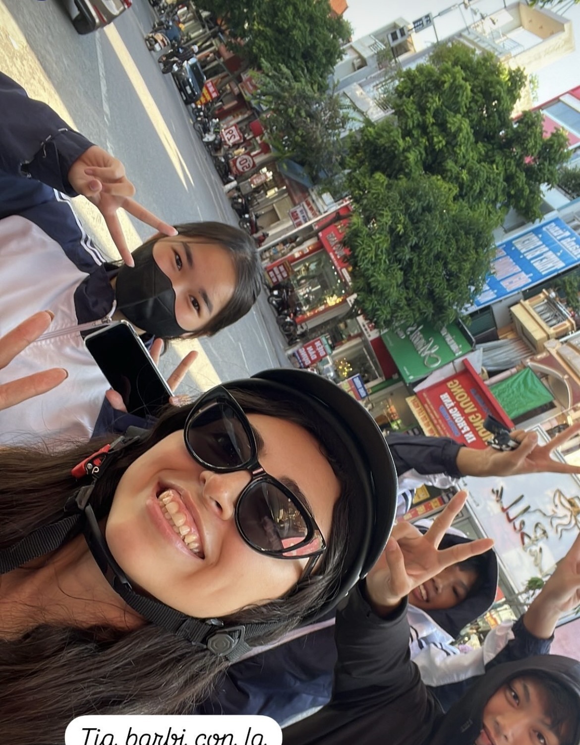Bárbara on a motorbike in Vietnam, helmet on, with her young Vietnamese students nearby