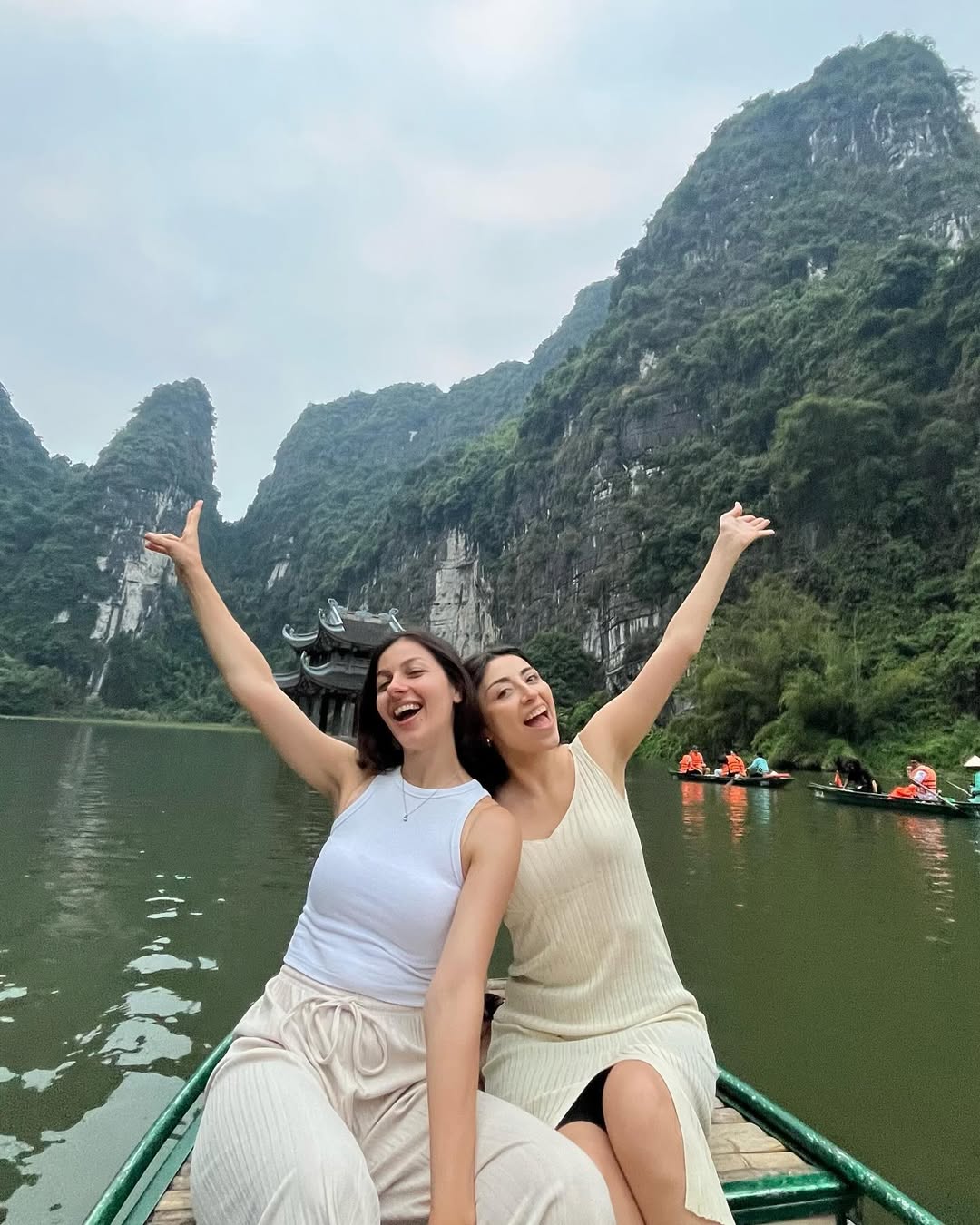 Bárbara and a friend on a boat in Trang An, Ninh Binh, arms raised in joy