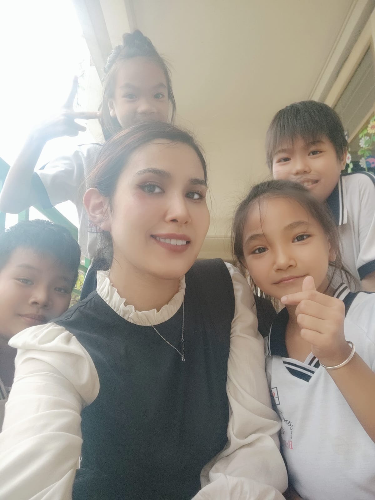 Female non-native English teacher close bond with Vietnamese students smiling selfie